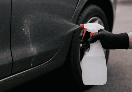 Han och sprayflaska mot en bil-lack